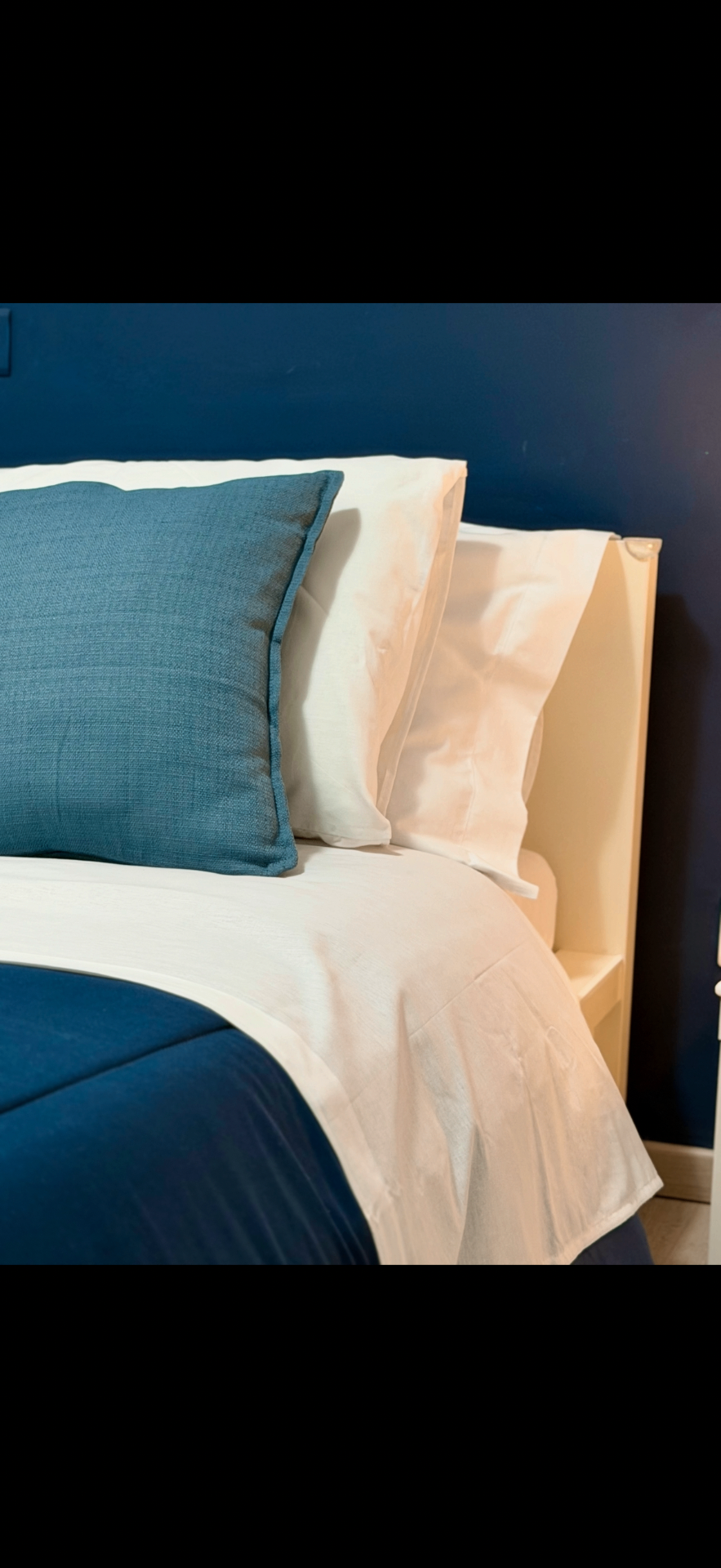 Crisp linens and blue accent pillow against deep blue wall in the main bedroom